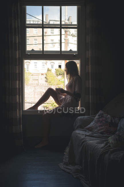 Mujer sentada cerca de la ventana mientras toma café en casa . - foto de stock