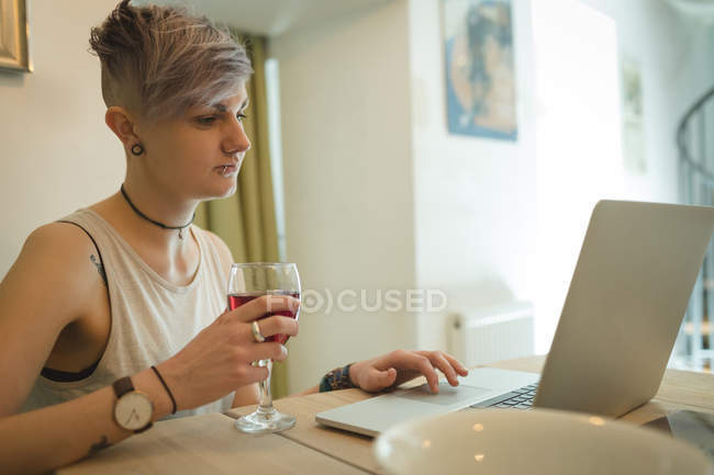 Женщина использует ноутбук, выпивая вино дома . — стоковое фото