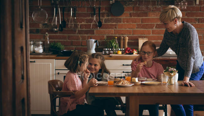 Бабушка и внучки завтракают за столом на кухне — стоковое фото