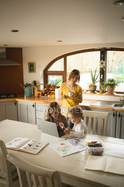 Мати дивиться, як діти використовують ноутбук на кухні вдома — стокове фото