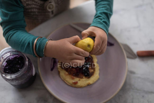 Vista cortada de menino espremendo limão em panquecas à mesa . — Fotografia de Stock