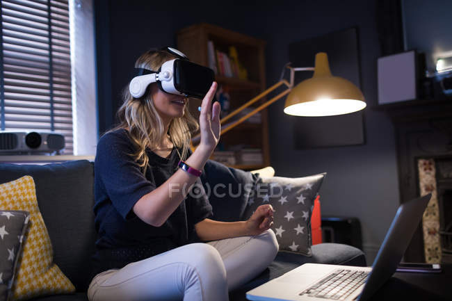 Mulher sentada no sofá e usando seu fone de ouvido de realidade virtual em casa — Fotografia de Stock