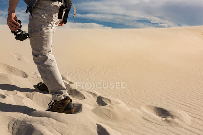 Low section of male hiker with binoculars walking on sand — Stock Photo