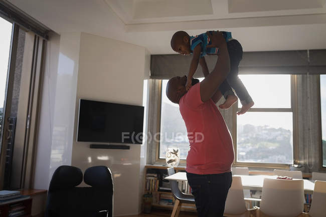 Pai levantando filho enquanto brincava na sala de estar em casa . — Fotografia de Stock