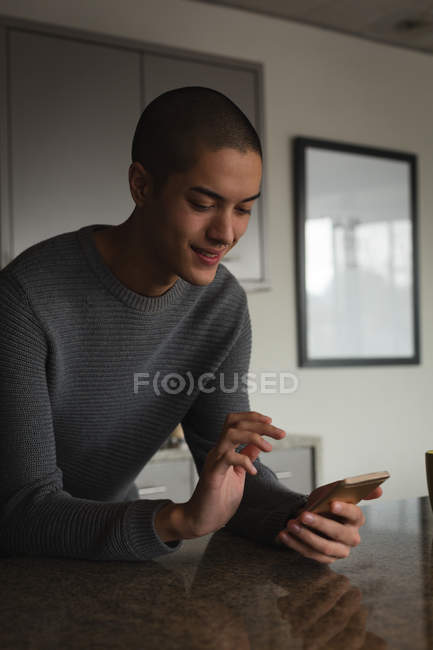Jeune homme heureux utilisant un téléphone portable à la maison — Photo de stock
