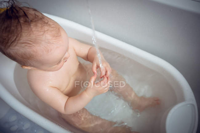 Baby girl playing with water in bathtub at home — Stock Photo