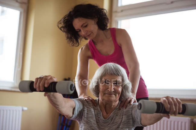 Terapeuta feminina assistindo mulher idosa com halteres em lar de idosos — Fotografia de Stock
