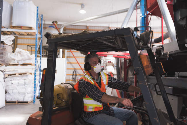 Homme en tenue de travail protectrice assis dans un chariot élévateur à l'usine — Photo de stock