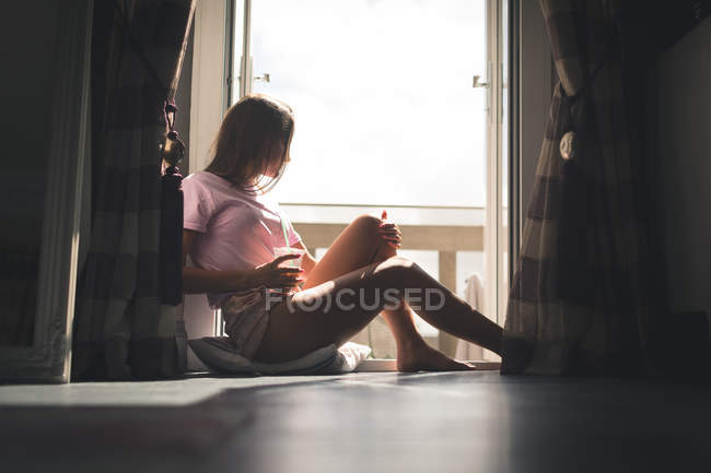 Frau sitzt am Fenster und trinkt Kaffee zu Hause. — Stockfoto