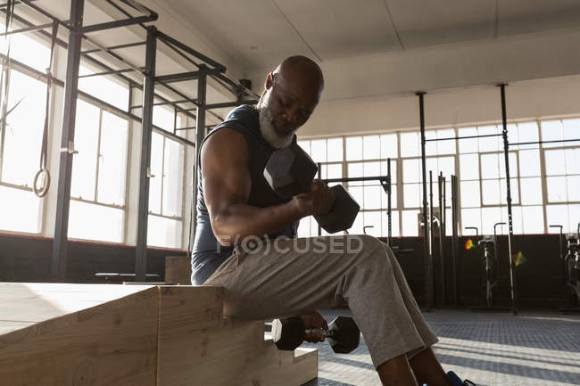 Homme âgé déterminé à faire de l'exercice avec des haltères dans la salle de fitness . — Photo de stock