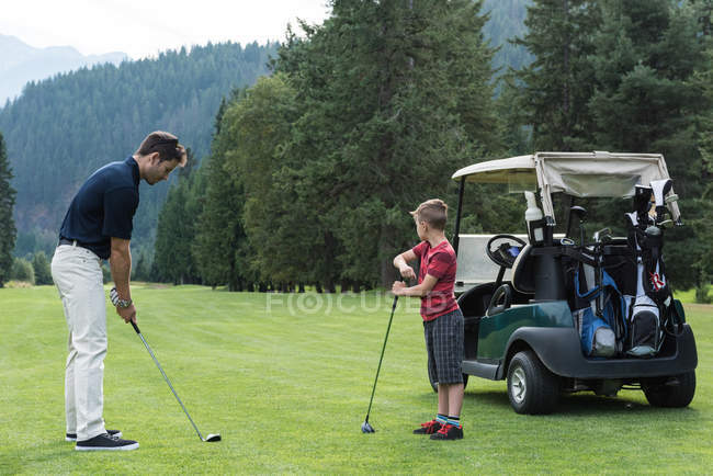 Padre ayudando a su hijo a jugar golf en el campo - foto de stock
