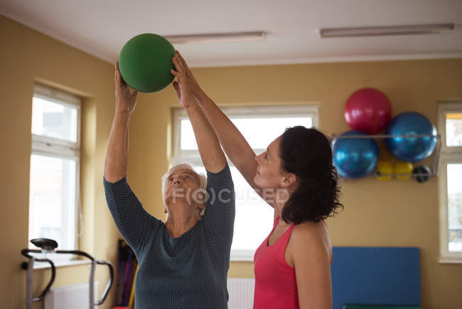 Female therapist assisting senior woman with exercise ball in nursing home — Stock Photo