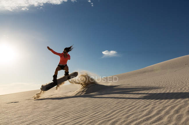 Mujer haciendo sandboard en una duna de arena en un día soleado - foto de stock
