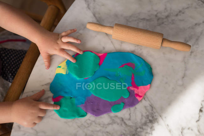 Mani del bambino che giocano con argilla colorata e mattarello a casa . — Foto stock