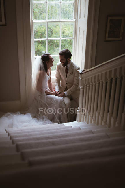 Happy bride and groom sitting on the window sill and laughing — Stock Photo