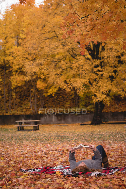 Woman lying down in the park and reading novel during autumn — Stock Photo