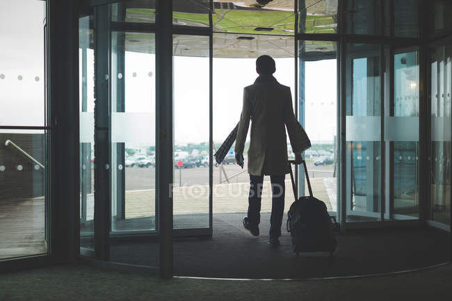 Вид ззаду бізнесмена, що виходить з готелю з багажем — стокове фото