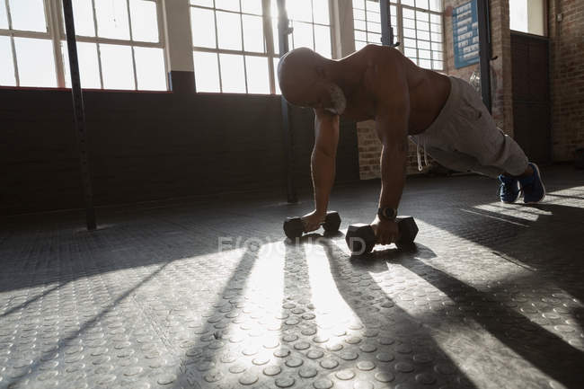 Homem sênior determinado fazendo push-up com halteres no estúdio de fitness . — Fotografia de Stock