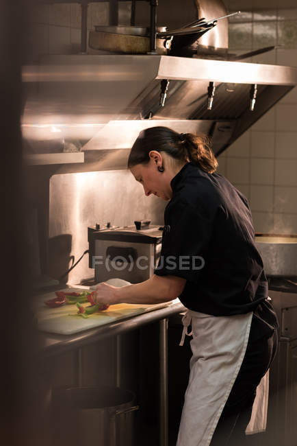 Вид ззаду шеф-кухаря нарізає овочі на комерційній кухні — стокове фото