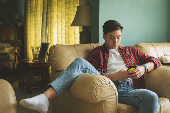 Hombre usando teléfono móvil en sillón en la sala de estar en casa . - foto de stock