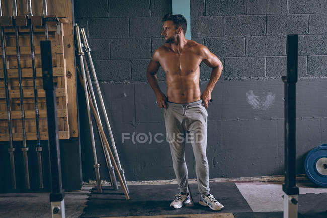 Решительный мускулистый человек, стоящий с руками на бедре в фитнес-студии — стоковое фото