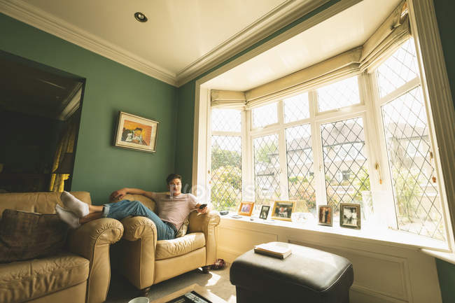 Чоловік тримає телевізійний пульт дистанційного керування на дивані у вітальні будинку . — стокове фото
