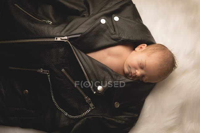 Новонароджена дитина спить в чорній шкіряній куртці на пухнастій ковдрі . — стокове фото