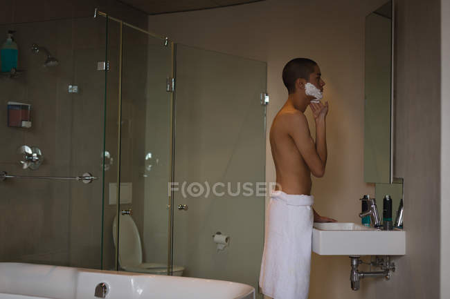 Junger Mann trägt im Badezimmer Rasierschaum auf sein Gesicht auf — Stockfoto