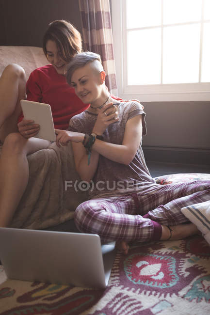 Pareja lesbiana usando tableta digital en la sala de estar en casa . - foto de stock