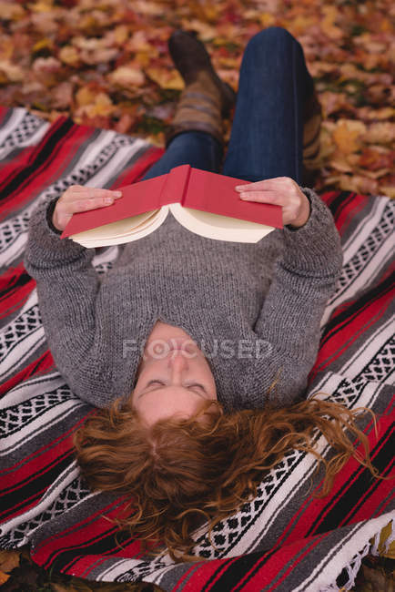 Beautiful woman lying down in the autumn park and reading novel — Stock Photo