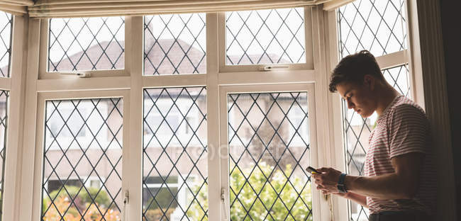 Человек, использующий мобильный телефон возле окна с сеткой дома . — стоковое фото