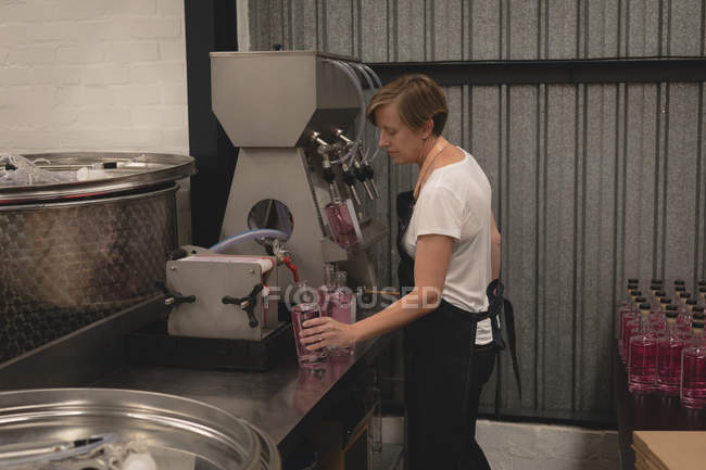 Gim de enchimento do trabalhador feminino na garrafa da máquina na fábrica — Fotografia de Stock
