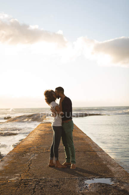 Casal romântico beijando enquanto estava de pé em um molhe durante o pôr do sol — Fotografia de Stock