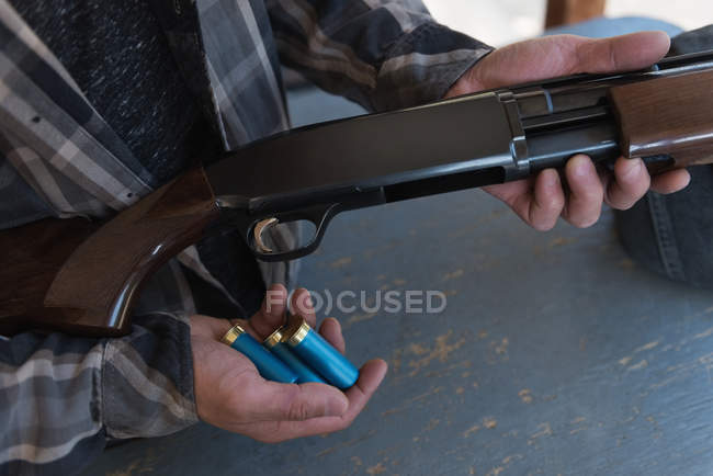 Mid section of man loading bullet into shotgun — Stock Photo