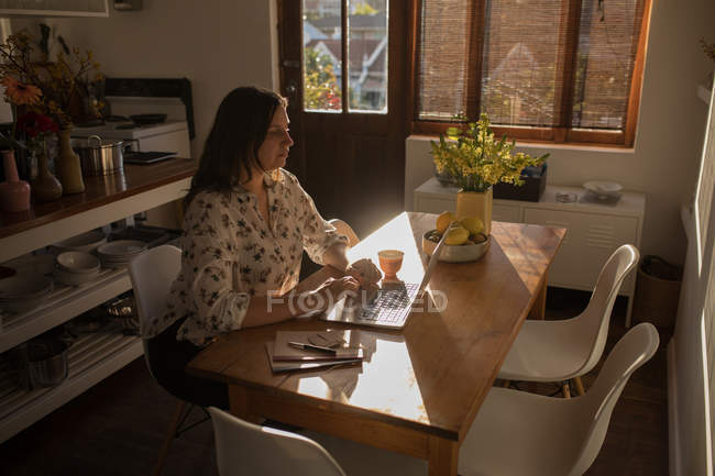 Mujer caucásica usando el ordenador portátil en la mesa en casa - foto de stock