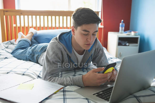 Mann benutzte Handy mit Laptop am Bett. — Stockfoto