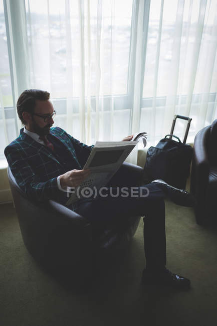 Empresário lendo jornal em cadeira de braço no hotel — Fotografia de Stock