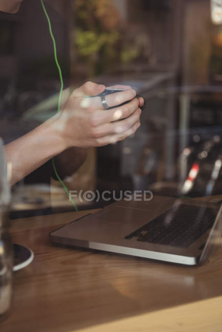 Sección media del hombre tomando café mientras usa el ordenador portátil en la cafetería - foto de stock