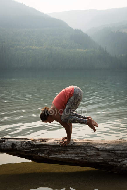 Side view of fit woman performing a hand stand on a fallen tree trunk — Stock Photo