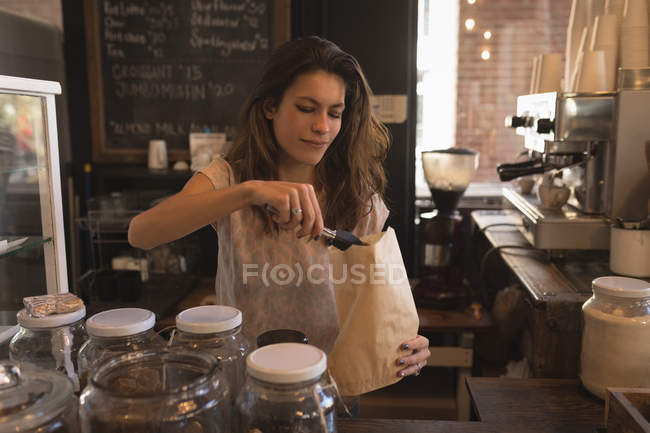 Официантка упаковывает сладкую еду в бумажный пакет у стойки в кафе — стоковое фото