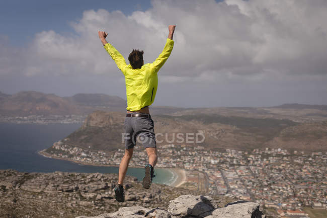 Hiker jumping on mountain peak on a sunny day — Stock Photo