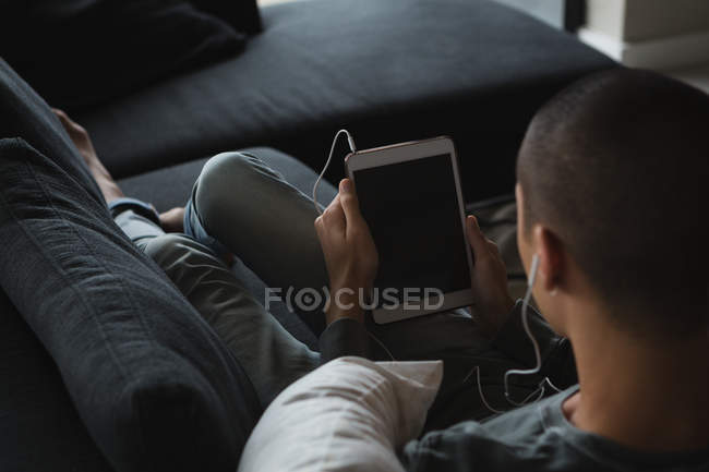Young man listening music on digital tablet in living room at home — Stock Photo