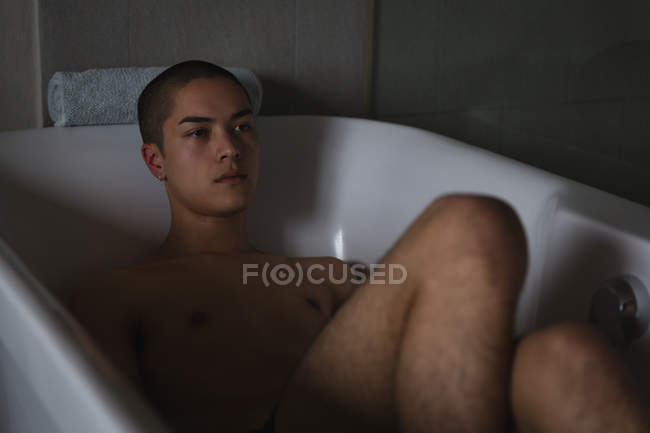 Thoughtful young man relaxing in bathtub at bathroom — Stock Photo