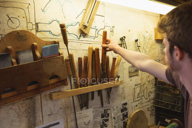 Мужской плотник снимая инструмент с стойки в мастерской — стоковое фото