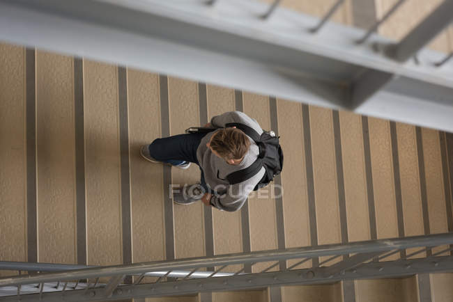 Vista de ángulo alto del estudiante universitario caminando con el ordenador portátil en la escalera - foto de stock