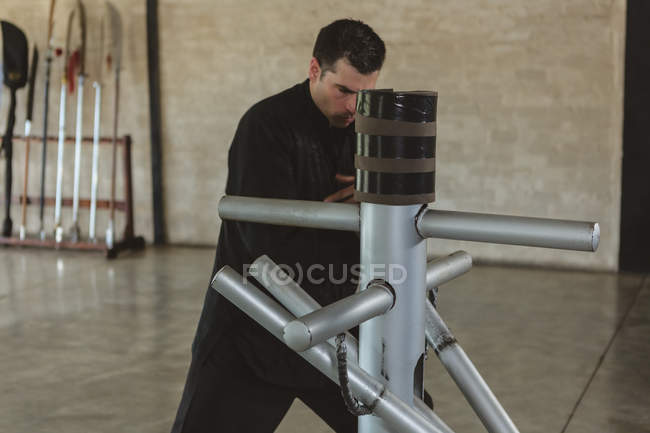 Karate fighter practicing with wooden dummy in fitness studio. — Stock Photo