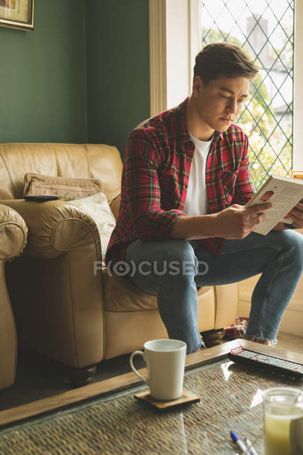 Чоловік читає книгу в кріслі у вітальні вдома . — стокове фото