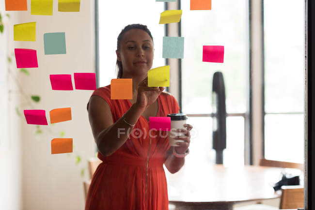 Female executive writing on sticky notes in office — Stock Photo