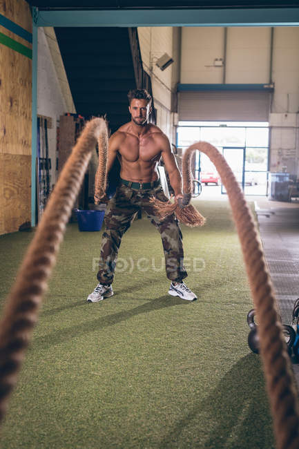 Uomo muscoloso determinato che si allena con la corda nella palestra — Foto stock