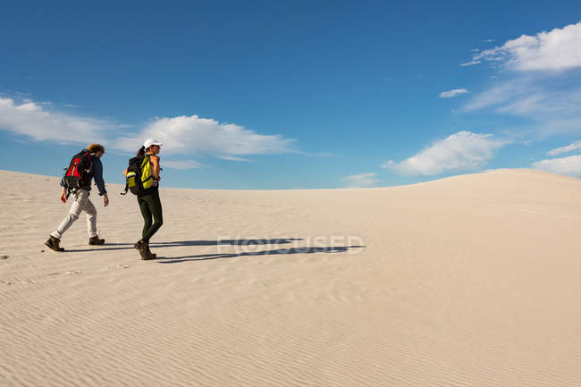 Pareja con mochila caminando sobre arena en un día soleado - foto de stock